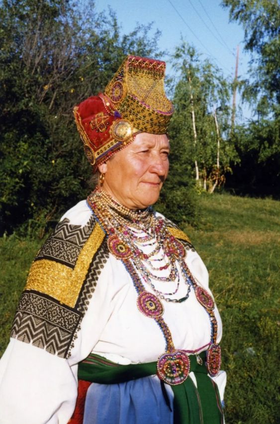 Rahvariietes naine. Peas punane-kuldne tanu, seljas rahvuslik valge pluus ja sinine seelik. 